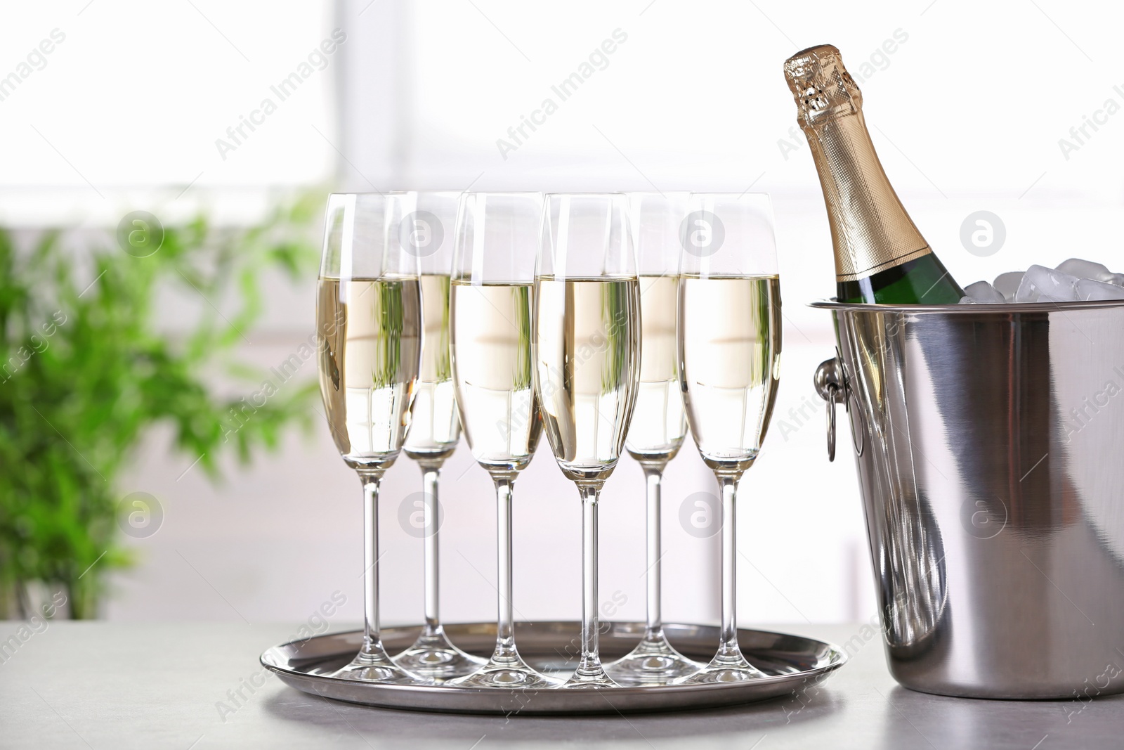 Photo of Glasses with champagne and bottle in bucket on table indoors