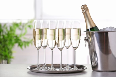 Photo of Glasses with champagne and bottle in bucket on table indoors