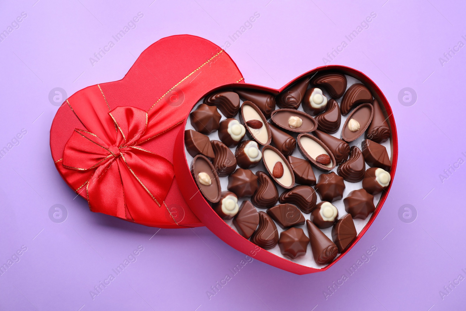 Photo of Heart shaped box with delicious chocolate candies on lilac background, top view