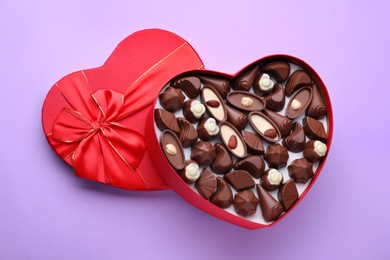 Heart shaped box with delicious chocolate candies on lilac background, top view