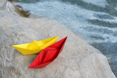 Photo of Beautiful yellow and red paper boats on stone near water outdoors, above view