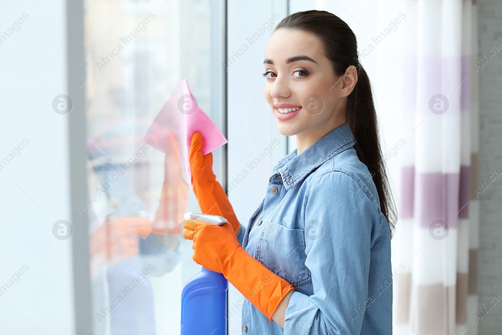 Photo of Young woman cleaning window glass at home