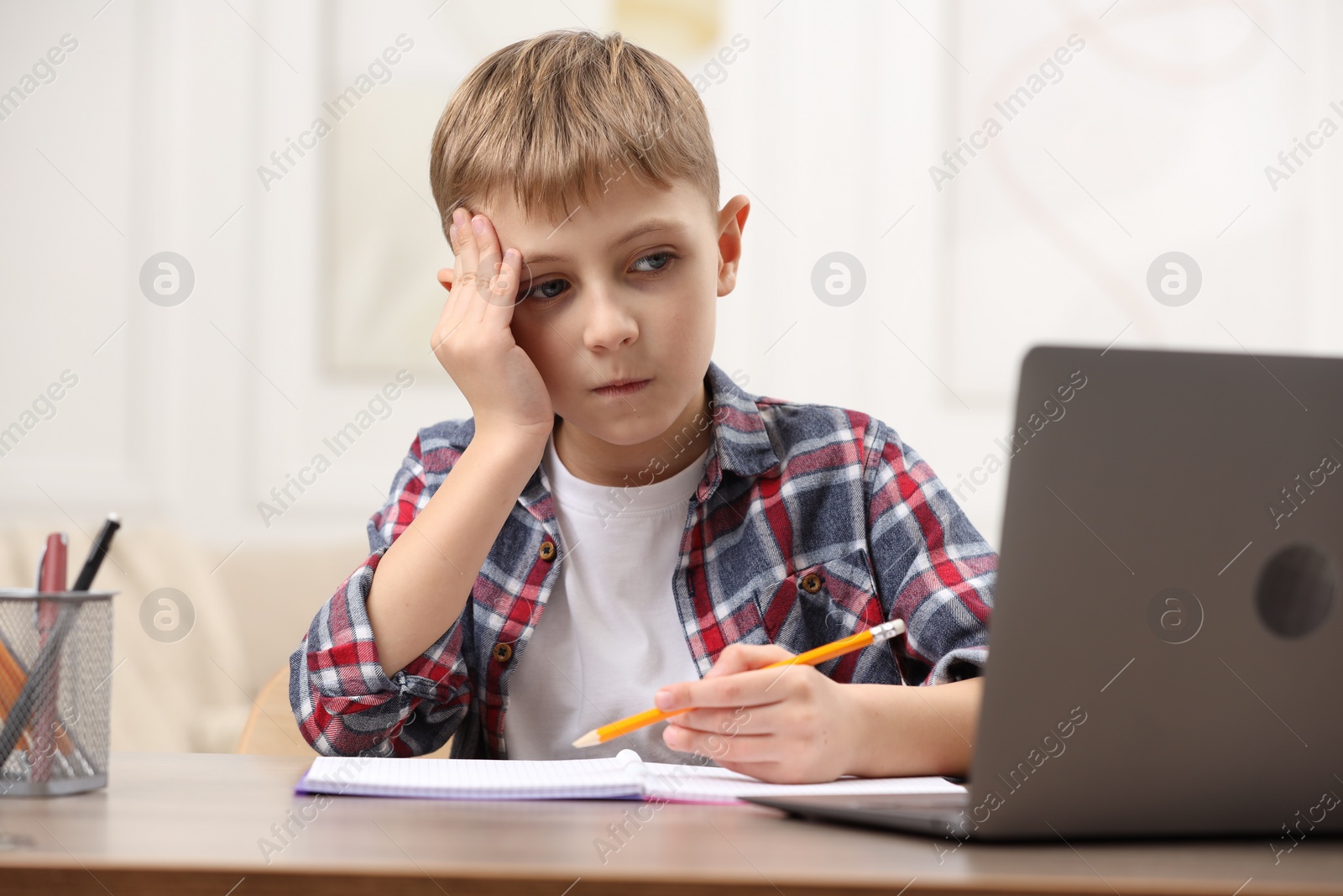 Photo of Little boy suffering from headache while studying at wooden desk indoors