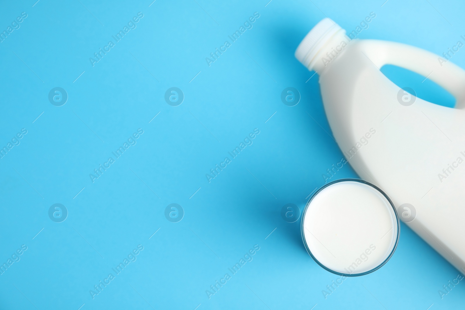 Photo of Gallon bottle and glass of milk on light blue background, flat lay. Space for text