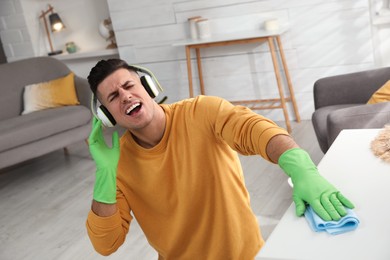 Photo of Man in headphones with rag singing while cleaning at home
