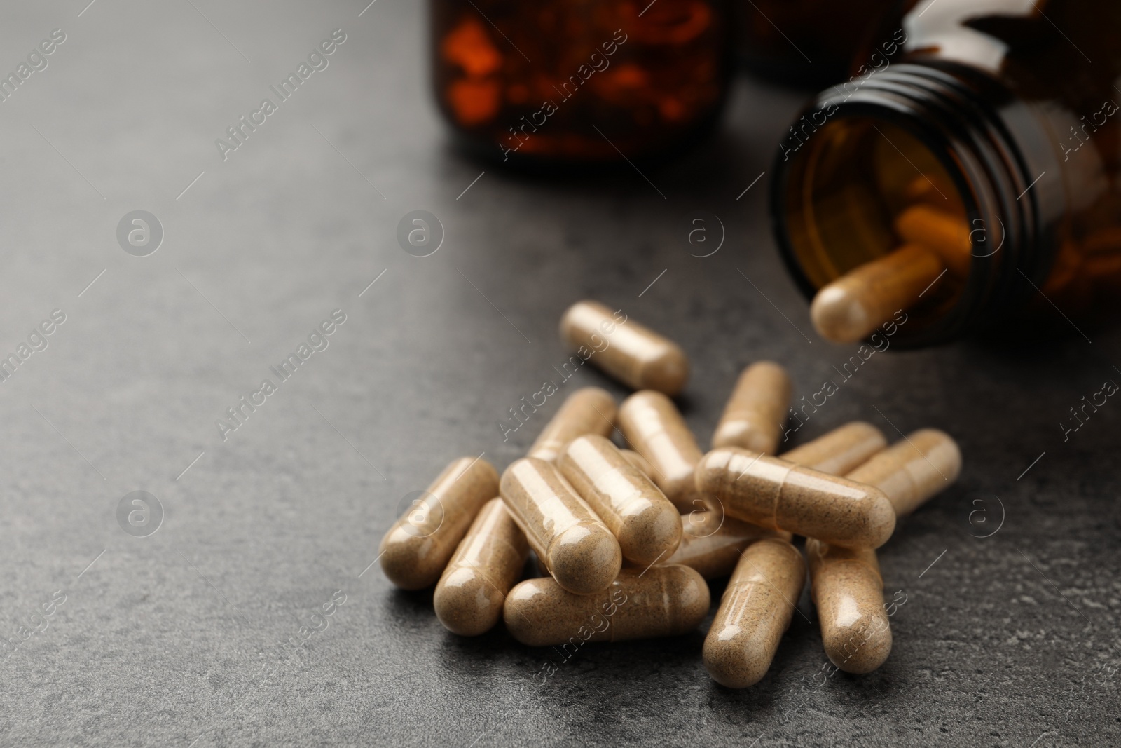 Photo of Overturned bottle with dietary supplement capsules on grey table, closeup. Space for text