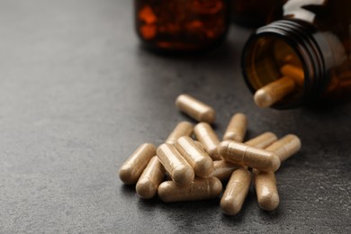 Overturned bottle with dietary supplement capsules on grey table, closeup. Space for text