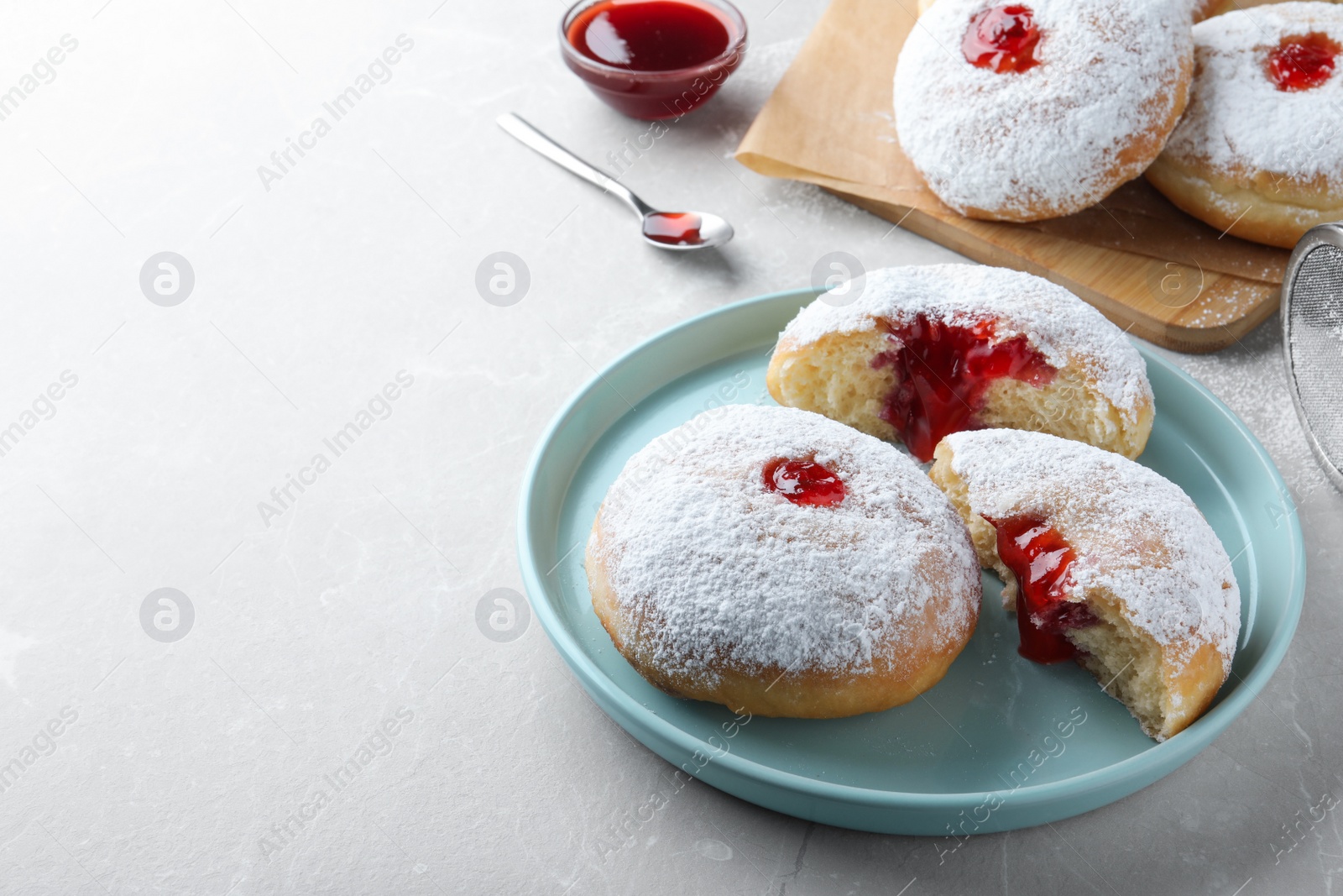 Photo of Delicious donuts with jelly and powdered sugar on light grey table. Space for text