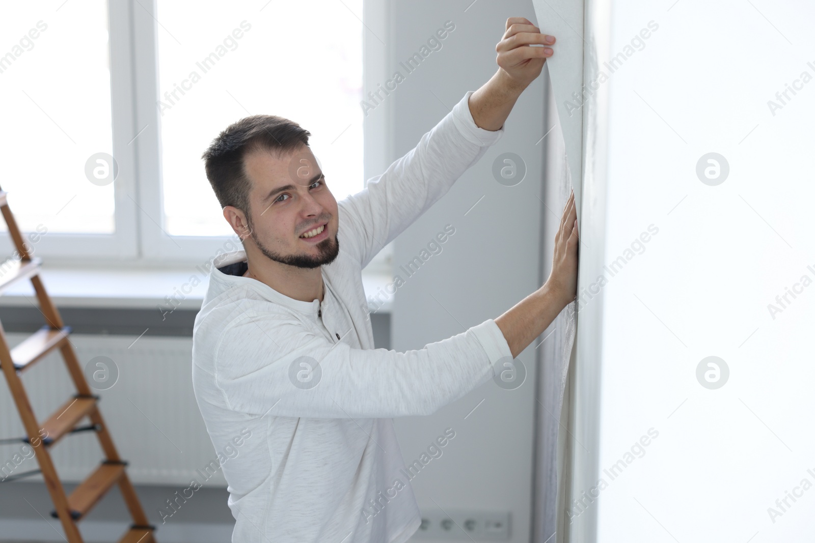 Photo of Man hanging stylish gray wallpaper in room