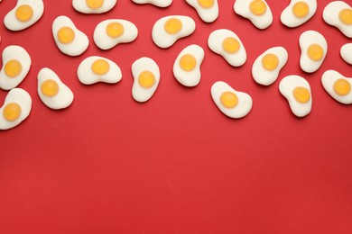 Photo of Tasty jelly candies in shape of egg on red background, flat lay. Space for text