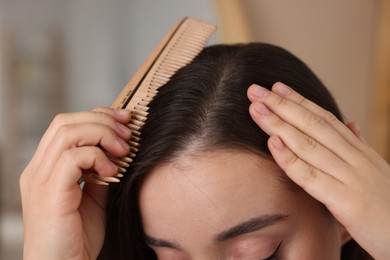 Photo of Woman with comb examining her hair and scalp on blurred background, closeup