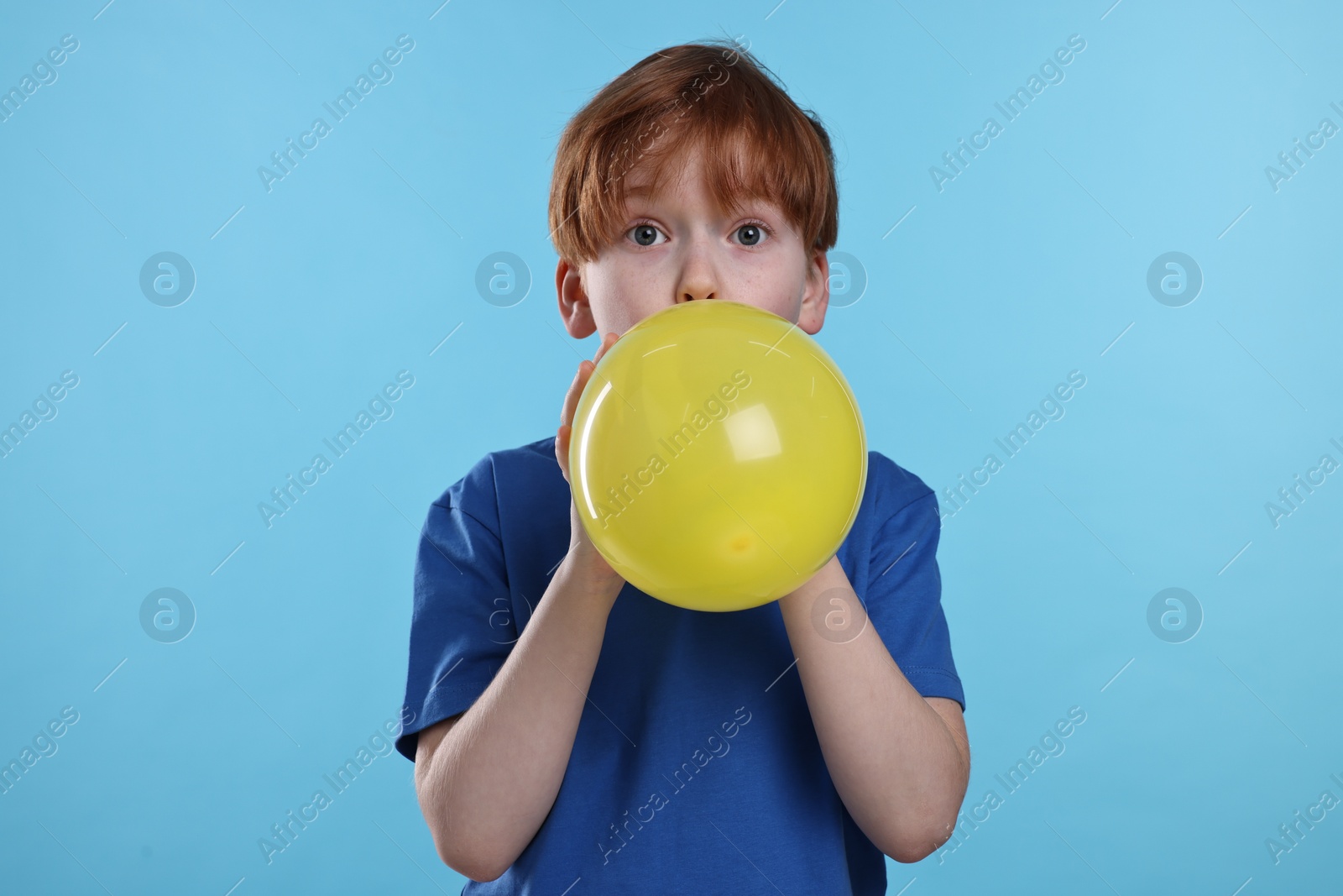 Photo of Boy inflating yellow balloon on light blue background