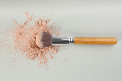 Photo of Makeup brush and scattered face powder on light grey background, top view