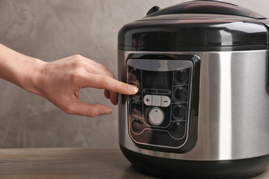 Photo of Woman turning on modern electric multi cooker on grey background, closeup