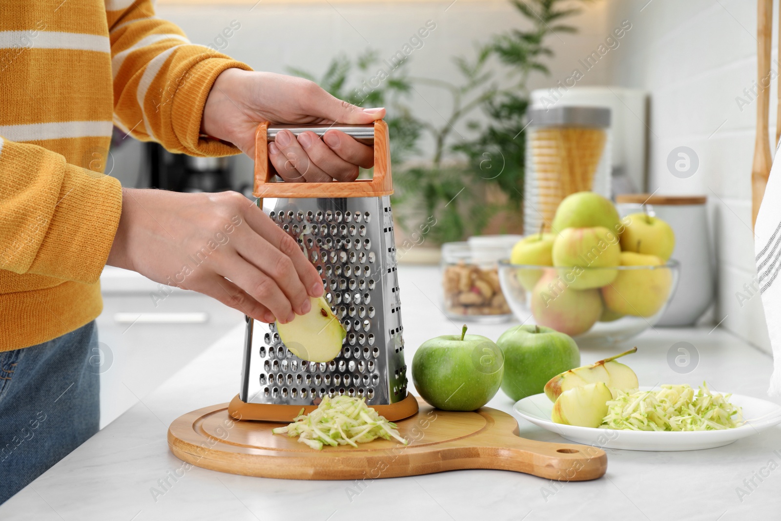 Photo of Woman grating fresh green apple at kitchen counter, closeup