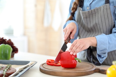 Photo of Professional female chef cutting pepper on table in kitchen, closeup