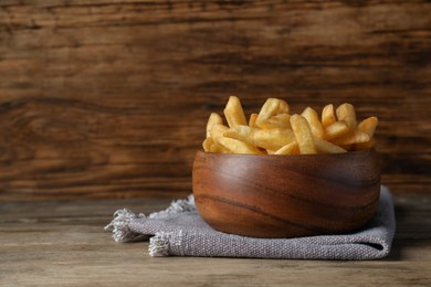 Photo of Delicious fresh french fries in bowl on wooden table, space for text