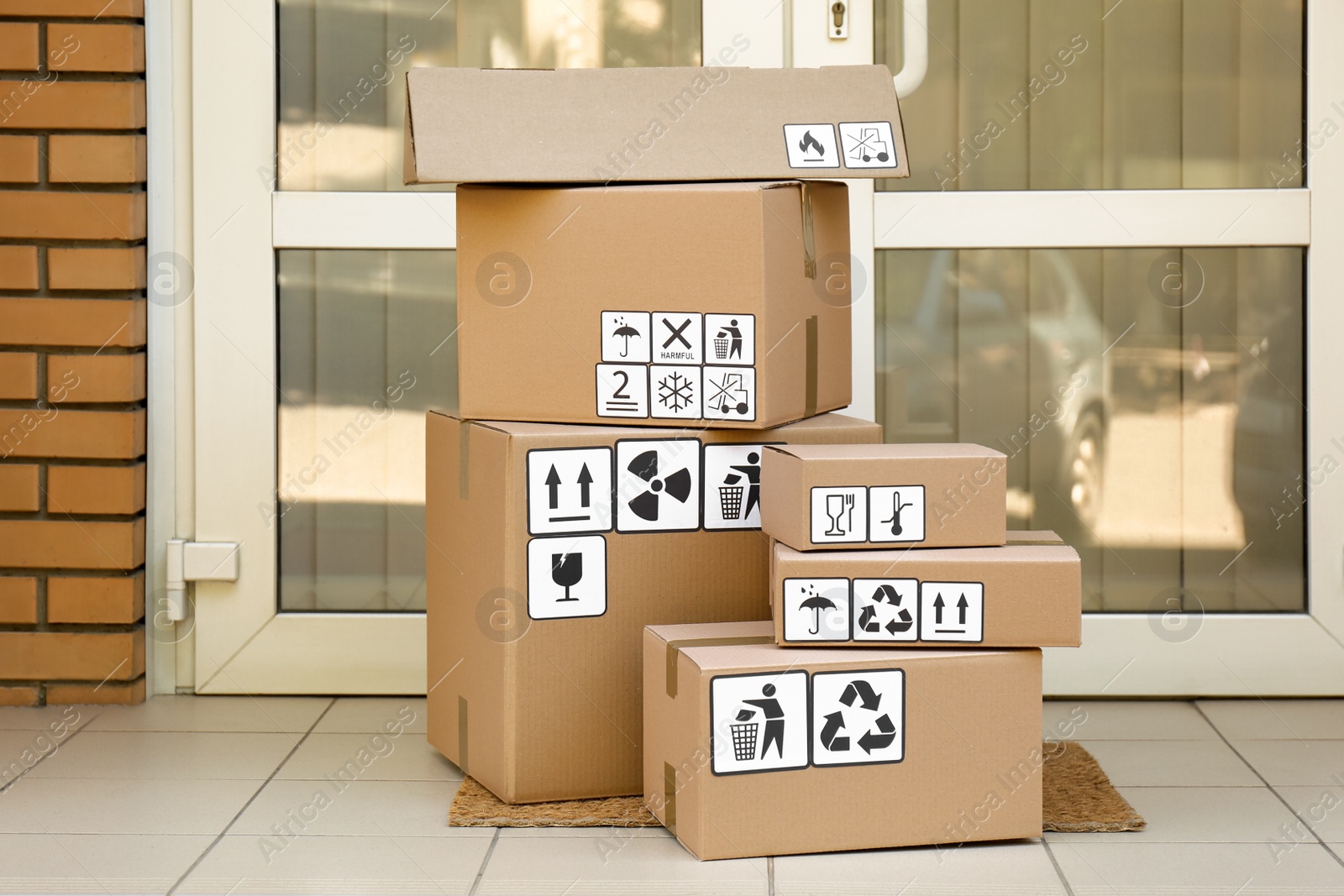 Photo of Cardboard boxes with different packaging symbols on door mat near entrance. Parcel delivery