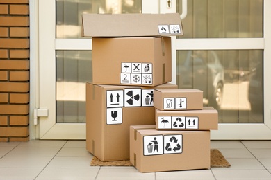 Cardboard boxes with different packaging symbols on door mat near entrance. Parcel delivery