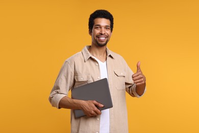 Happy man with laptop showing thumb up on orange background