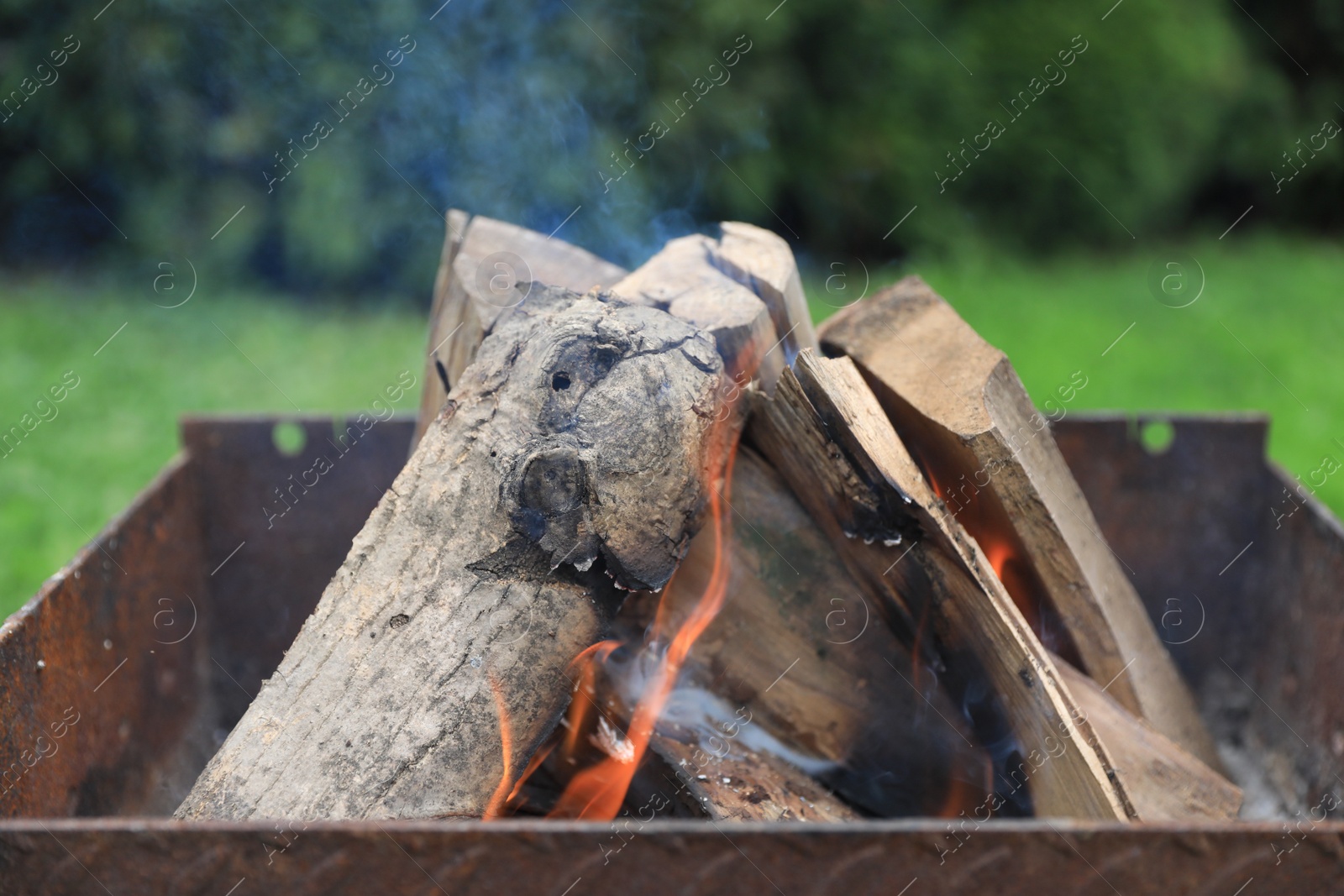 Photo of Metal brazier with burning firewood outdoors, closeup