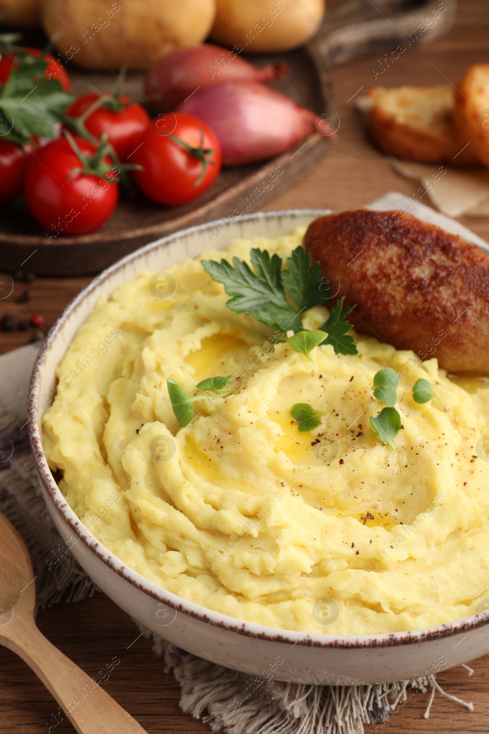 Photo of Bowl of tasty mashed potatoes with parsley, black pepper and cutlet served on wooden table, closeup