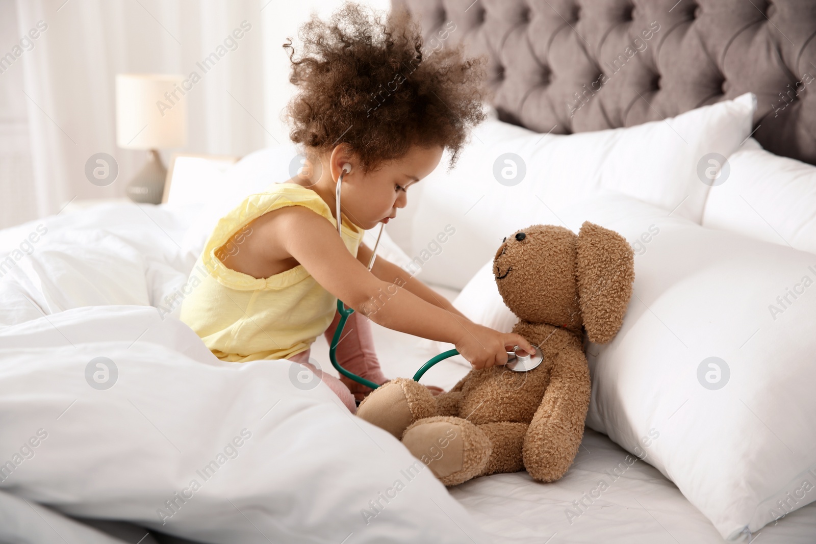 Photo of Cute African American child imagining herself as doctor while playing with stethoscope and toy bunny at home