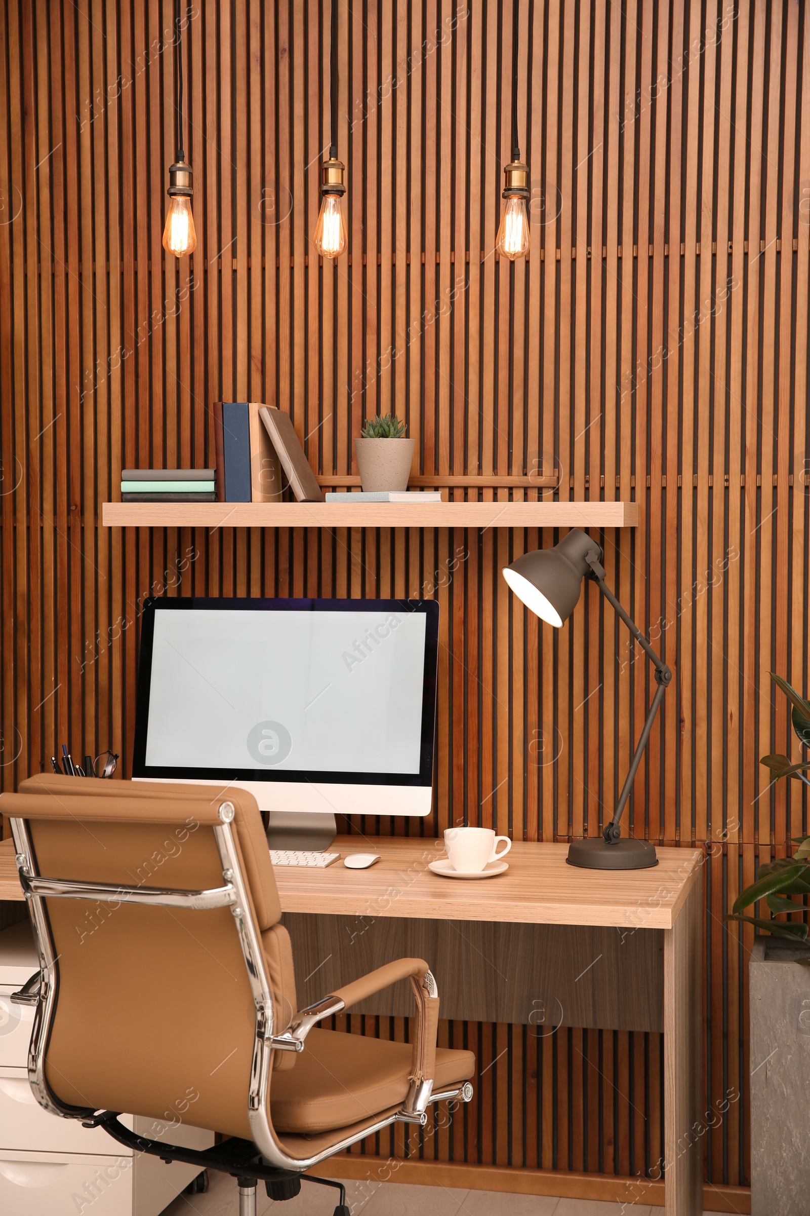 Photo of Comfortable workplace with computer near wooden wall in stylish room interior. Home office design