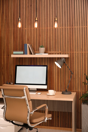 Photo of Comfortable workplace with computer near wooden wall in stylish room interior. Home office design