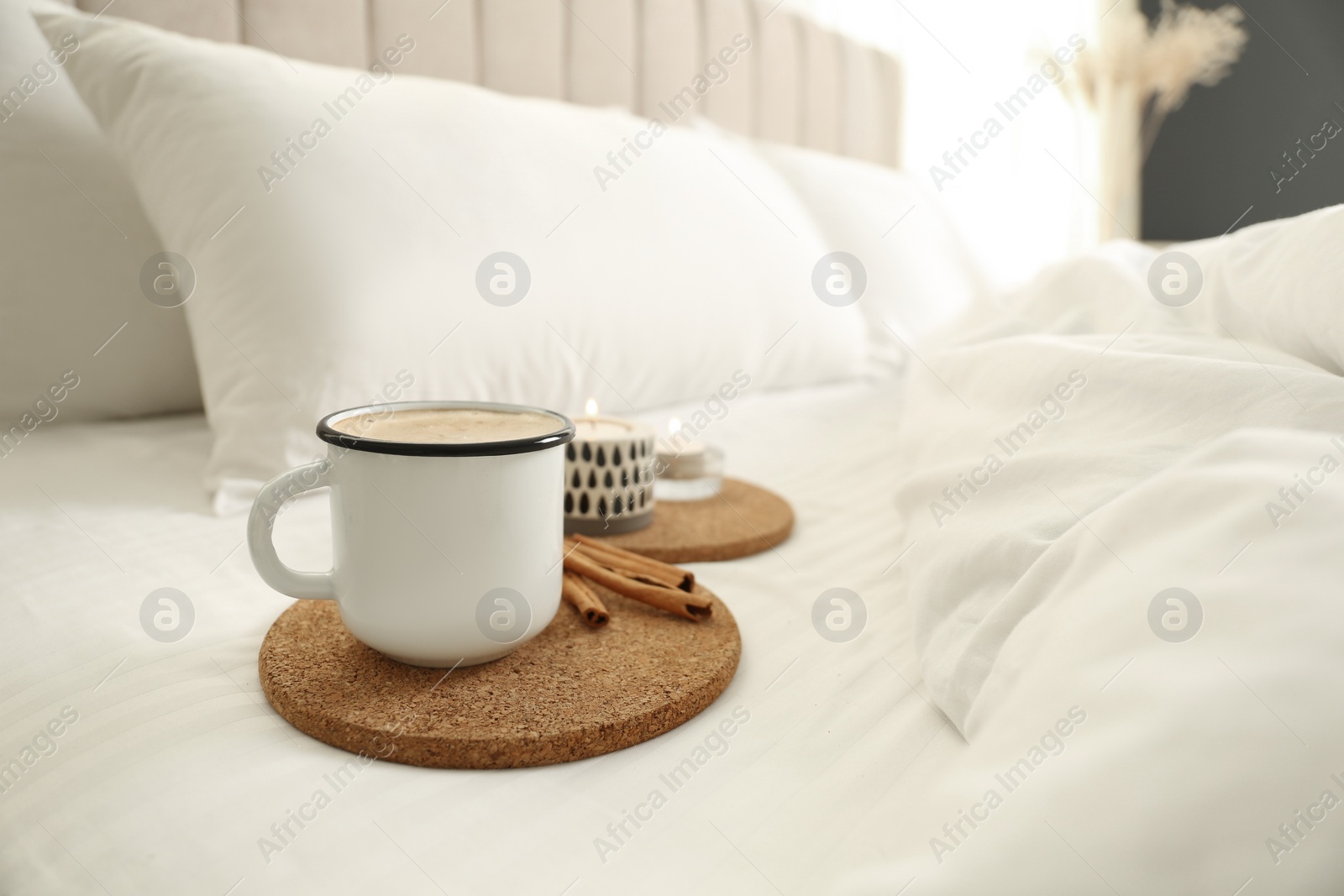 Photo of Cup of aromatic coffee and cinnamon sticks on bed with soft blanket, closeup. Space for text