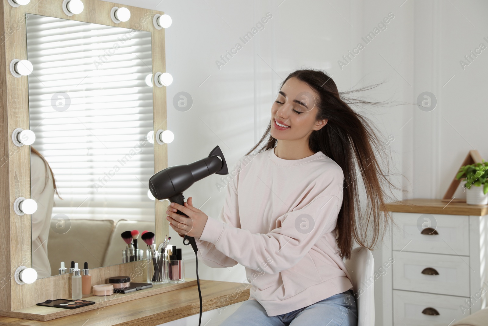 Photo of Beautiful young woman using hair dryer near mirror at home