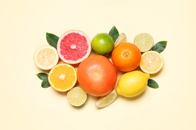 Different cut citrus fruits and leaves on beige table, flat lay