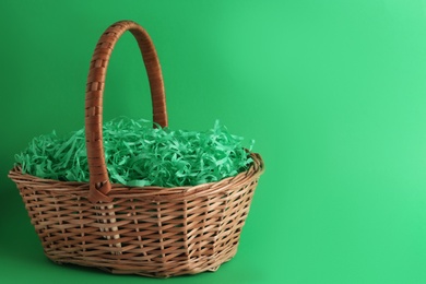 Photo of Easter basket with bright paper filler on green background, space for text