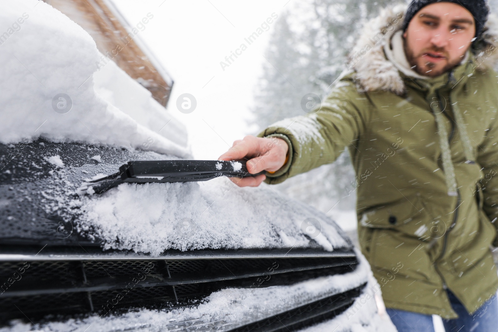 Photo of Young man cleaning snow from car outdoors on winter day