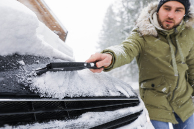 Photo of Young man cleaning snow from car outdoors on winter day