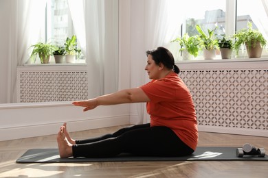 Photo of Overweight mature woman stretching on floor at home