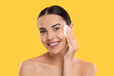 Photo of Beautiful woman removing makeup with cotton pad on yellow background