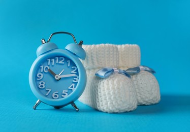 Alarm clock and baby booties on light blue background. Time to give birth