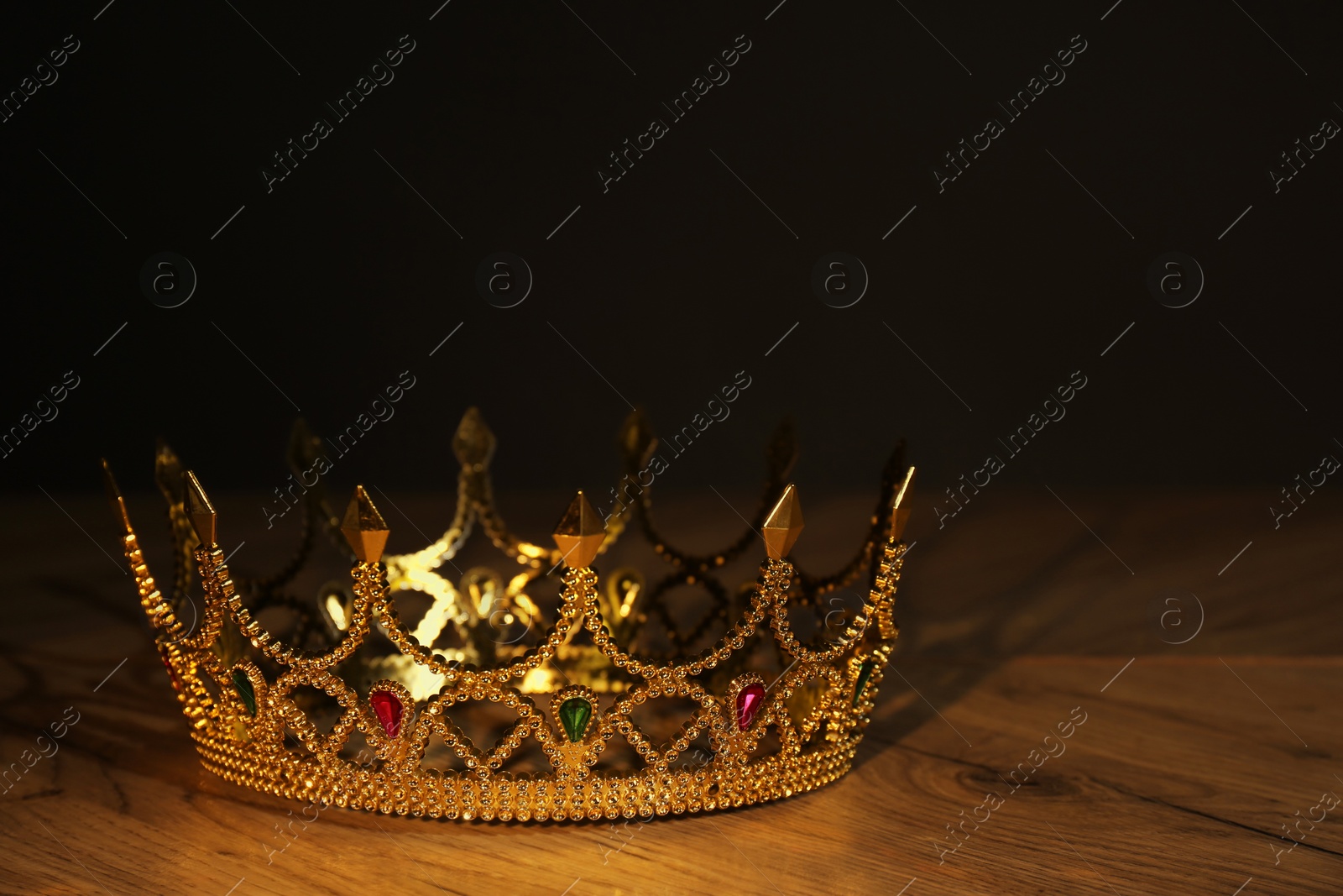 Photo of Beautiful golden crown with gems on wooden table. Fantasy item