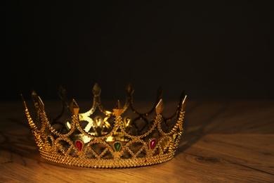 Photo of Beautiful golden crown with gems on wooden table. Fantasy item