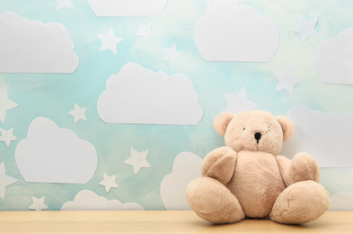 Photo of Teddy bear on white wooden table near wall with blue sky, space for text. Baby room interior