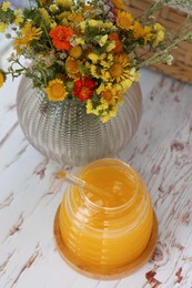Photo of Delicious fresh honey and beautiful flowers on white wooden table indoors