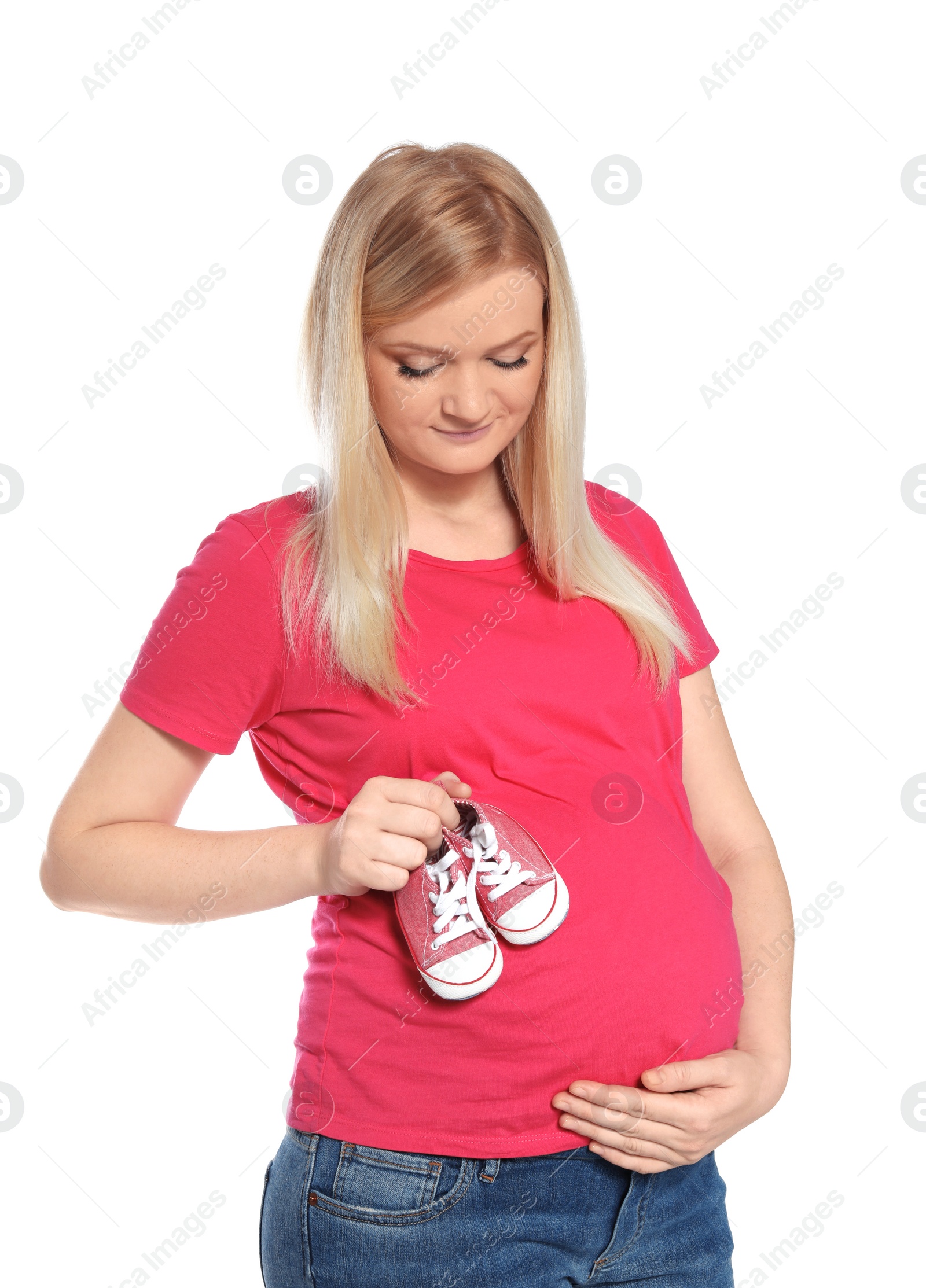 Photo of Beautiful pregnant woman holding baby booties near tummy on white background