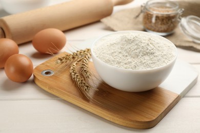 Photo of Bowl of flour, wheat ears and eggs on white wooden table
