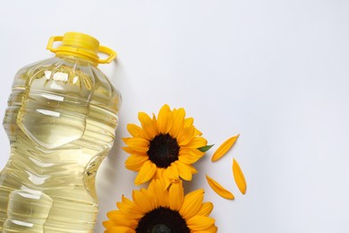 Photo of Bottle of cooking oil and sunflowers on white table, flat lay. Space for text