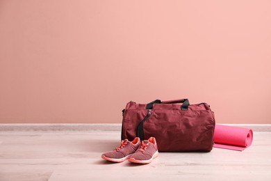 Photo of Red sports bag, sneakers and yoga mat on floor near pink wall, space for text