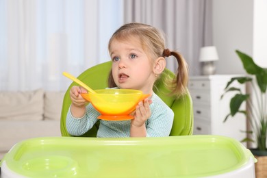 Photo of Cute little child with bowl of tasty yogurt in high chair indoors