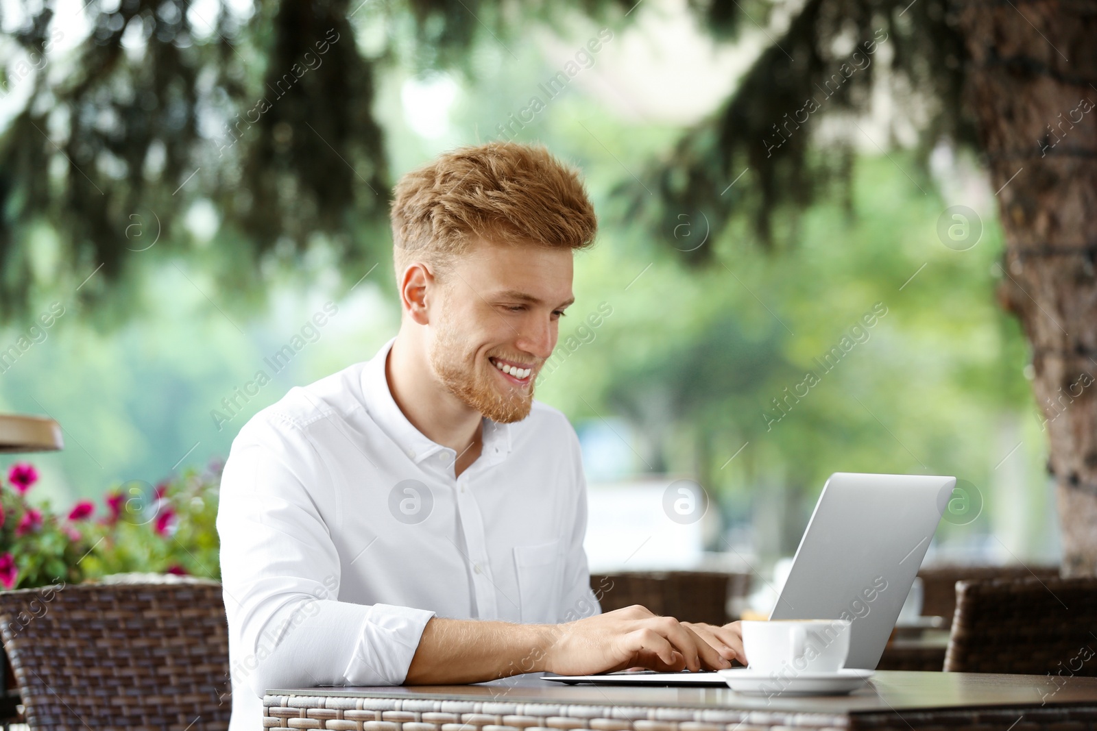 Photo of Young man working on laptop at table in cafe