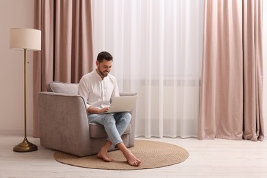Photo of Smiling man holding laptop on armchair near window with beautiful curtains at home. Space for text