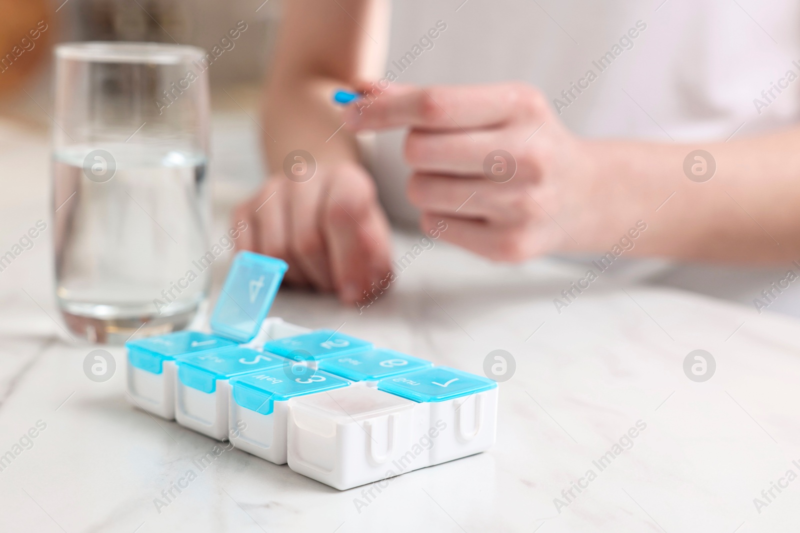 Photo of Woman with pills, organizer and glass of water at white marble table, selective focus